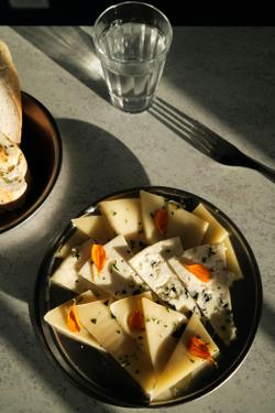 Elegant cheese platter garnished with edible flowers and herbs on a sunlit table.