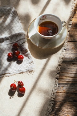 A cup of tea and some cherries on a table