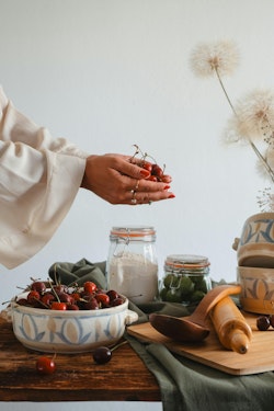 A woman is holding a bowl of cherries and a bowl of other food