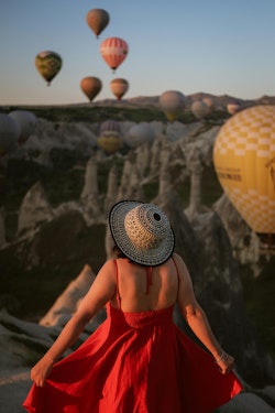 A woman in a red dress is looking at hot air balloons