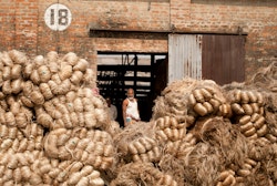 Worker Standing Behind Jute Fibres in Factory