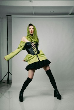 A woman in a green hoodie and black boots posing