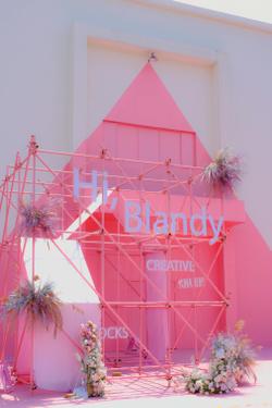 Vibrant pink art structure with floral accents at an outdoor event.