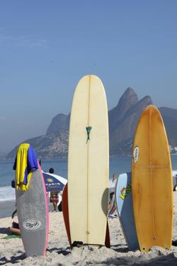 Colorful surfboards stand on Ipanema Beach with the Dois Irmãos mountains in the background.