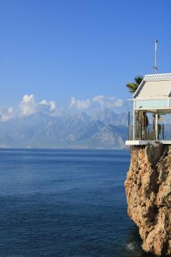 Stunning view of a house on a cliff by the sea against the Taurus Mountains in Antalya, Türkiye.