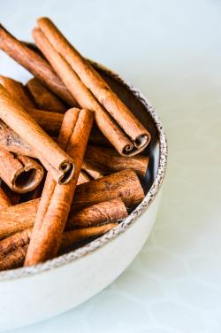 Aerial view of cinnamon sticks in a textured bowl on a light background.