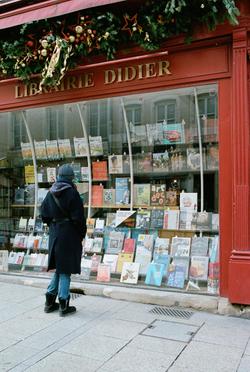 Person browsing the window display at Librairie Didier in Nancy, France.