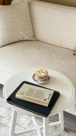 White table with a coffee cup, book, and tablet in a cozy living room setting.