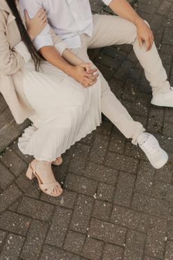 Stylish young couple sitting outdoors on paved ground wearing beige and white casual attire.