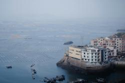 A scenic view of a coastal fishing village overlooking extensive sea farms. Calm and serene atmosphere.