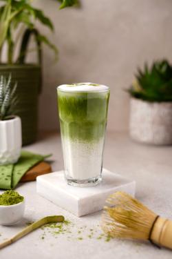 Refreshing iced matcha latte on marble slab with a bamboo whisk, surrounded by plants.