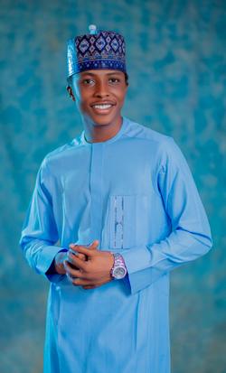 Smiling young man in traditional blue attire with intricate cap, studio portrait.