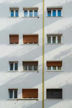 Minimalistic facade of a white apartment building with symmetrical windows and shutters.