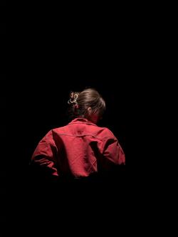 A lone individual in a red jacket captured from behind, set against a black background.
