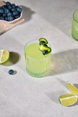 Lime juice with cucumber and blueberry garnish on a concrete surface, ideal for summer refreshment.