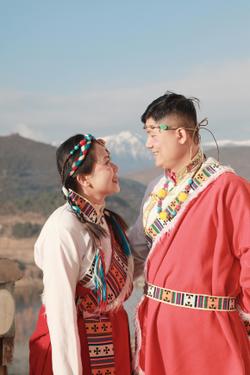 A joyful couple in vibrant traditional attire enjoying a scenic mountain view on a sunny day.