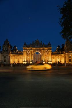 A yellow taxi passes in front of the illuminated Dolmabahçe Palace in İstanbul at night.