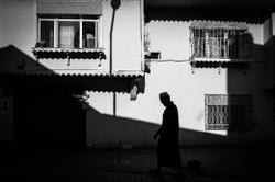 A black and white photo of a solitary man walking, casting shadows on Bursa's walls.