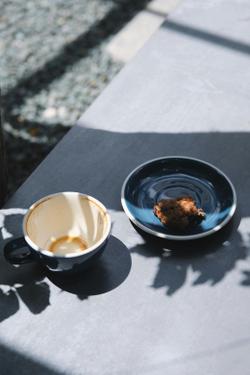 A blue coffee cup and dessert plate with a cookie in sunlight casting shadows.