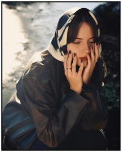 Thoughtful woman in a scarf and jacket sitting by a sunlit outdoors area in Rosario.