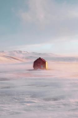 A red cabin stands solitary on a snowy landscape during sunrise, enveloped by soft pastel skies.