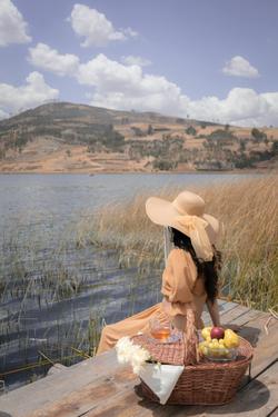 Woman in hat enjoying a lakeside picnic with a scenic mountain view. Ideal for summer lifestyle themes.