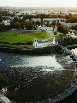 Aerial shot of a river, lush greenery, and buildings in County Clare, Ireland at sunset.