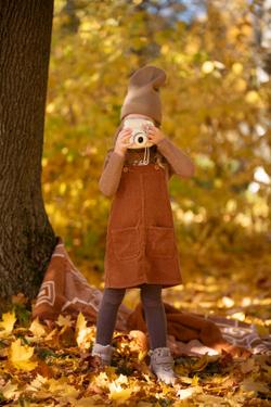 A young girl in autumn attire photographs a vibrant forest, capturing the essence of fall.