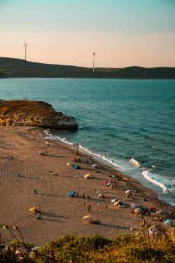 A coastal view in Kırklareli, Türkiye, featuring a busy beach and wind turbines under clear skies.