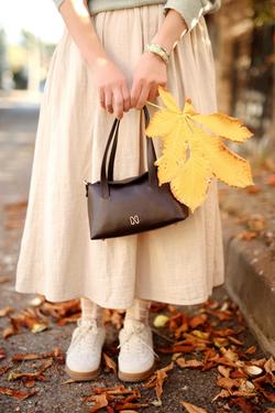 Stylish autumn outfit with a yellow leaf and handbag on a leafy street.