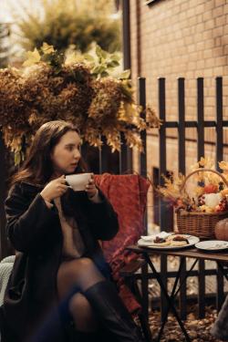 A woman enjoying coffee outdoors in an autumn setting with a basket and treats.