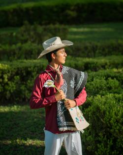A man wearing traditional Mexican attire holding a flower outdoors, showcasing vibrant cultural heritage.