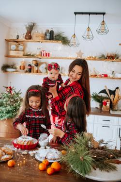 Mother and daughters baking in a festive kitchen, surrounded by holiday decorations.