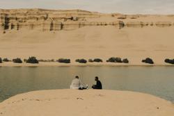 Two people enjoying a peaceful picnic by a serene lake in a desert landscape.